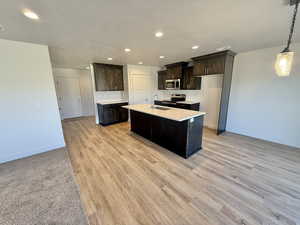 Kitchen featuring recessed lighting, light countertops, dark brown cabinets, a center island with sink, and stainless steel appliances