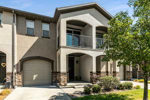 View of front of property with stone siding, a balcony, driveway, and stucco siding