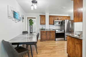 Kitchen with stainless steel appliances, light wood-style floors, light stone countertops, decorative backsplash, and brown cabinets