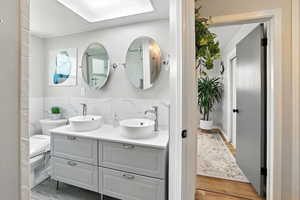 Bathroom with double vanity, tile walls, and wood finished floors