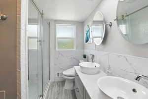 Full bathroom featuring tile walls, wainscoting, a shower stall, double vanity, and wood finished floors