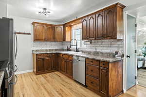 Kitchen with a textured ceiling, decorative backsplash, stainless steel appliances, light wood finished floors, and dark countertops