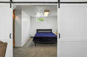 Bedroom featuring a barn door, carpet floors, and a textured ceiling