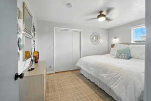 Bedroom with a closet, ceiling fan, light carpet, and a textured ceiling