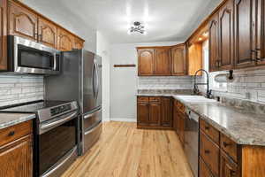 Kitchen with decorative backsplash, stainless steel appliances, a textured ceiling, and light wood-style floors