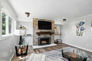 Living area featuring wood finished floors, a textured ceiling, a stone fireplace, and ornamental molding