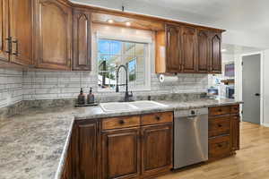 Kitchen with stainless steel dishwasher, light wood-style floors, tasteful backsplash, and dark countertops