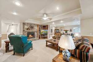 Living room with a textured ceiling, carpet, a stone fireplace, a tray ceiling, and recessed lighting