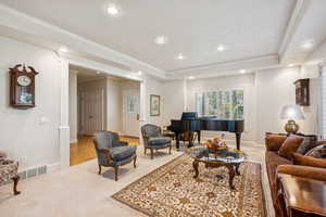 Living room with ornamental molding, light colored carpet, recessed lighting, and a tray ceiling