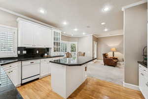 Kitchen with ornamental molding, light wood-style floors, white dishwasher, white cabinetry, and decorative backsplash