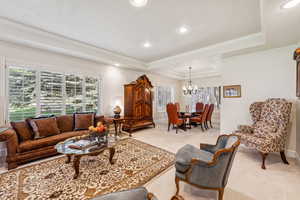 Living area featuring a raised ceiling, ornamental molding, recessed lighting, light colored carpet, and a chandelier