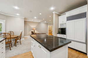 Kitchen with paneled refrigerator, ornamental molding, a kitchen island, light wood-style floors, and white cabinets