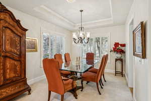 Dining space with light carpet, a tray ceiling, and a chandelier
