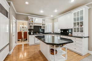 Kitchen featuring open shelves, backsplash, white cabinetry, crown molding, and premium range hood