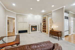 Living area featuring light colored carpet, crown molding, a fireplace, and recessed lighting