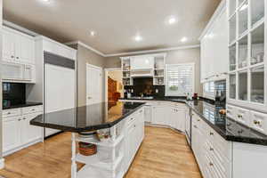 Kitchen with open shelves, tasteful backsplash, white cabinets, light wood finished floors, and paneled built in refrigerator