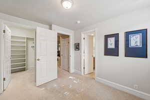 Unfurnished bedroom featuring a walk in closet, light colored carpet, a textured ceiling, and ensuite bathroom