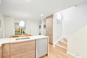 Kitchen with stacked washer and clothes dryer, modern cabinets, stainless steel dishwasher, light wood-style flooring, and light countertops