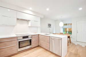 Kitchen with modern cabinets, stainless steel appliances, a peninsula, recessed lighting, and light countertops