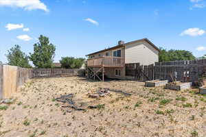 Rear view of house featuring a fenced backyard, a wooden deck, a chimney, and a garden