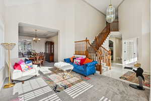 Tiled living area with a chandelier, a high ceiling, crown molding, a raised ceiling, and stairway