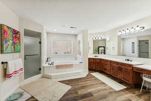 Bathroom with a bath, double vanity, a shower stall, and dark wood-style flooring