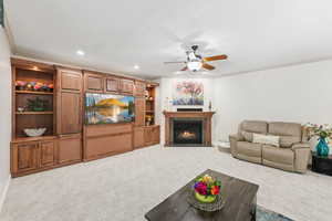 Living room with carpet, crown molding, a fireplace with flush hearth, a ceiling fan, and recessed lighting