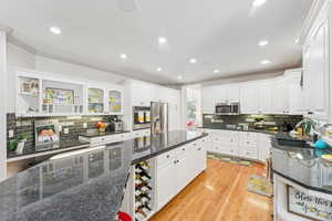Kitchen with backsplash, light wood finished floors, crown molding, white cabinetry, and recessed lighting