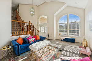 Carpeted living area featuring a chandelier, stairway, and high vaulted ceiling