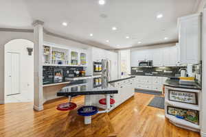 Kitchen featuring open shelves, crown molding, white cabinets, dark stone countertops, and light wood-style floors
