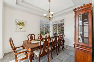 Dining area featuring a raised ceiling, light colored carpet, a chandelier, and ornamental molding