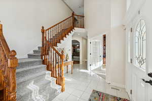Entrance foyer with arched walkways, light tile patterned floors, a towering ceiling, and stairs
