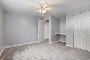 Unfurnished bedroom with carpet flooring, a closet, a ceiling fan, and an office area