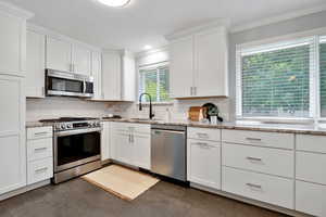 Kitchen featuring appliances with stainless steel finishes, ornamental molding, white cabinetry, and light stone countertops