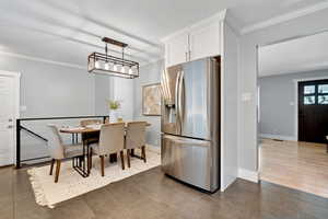 Kitchen with ornamental molding, stainless steel fridge with ice dispenser, and white cabinets