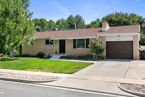 Ranch-style house featuring a garage, concrete driveway, a front lawn, and brick siding