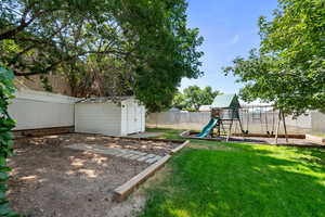 Fenced backyard featuring a storage unit and a playground