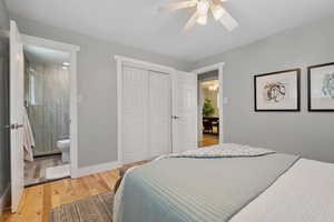 Bedroom with light wood-style floors, a closet, ensuite bath, and a ceiling fan