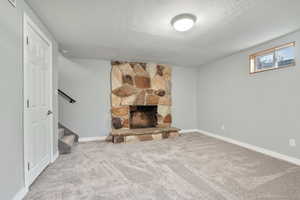 Basement featuring a textured ceiling, carpet floors, a stone fireplace, and stairway
