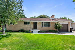 Single story home with a garage, brick siding, driveway, and a front yard