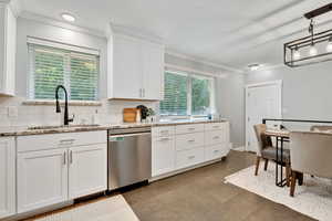 Kitchen featuring ornamental molding, stainless steel dishwasher, white cabinets, decorative backsplash, and light stone countertops