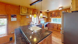 Kitchen with appliances with stainless steel finishes, decorative light fixtures, light wood-style floors, brown cabinets, and a peninsula