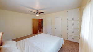Bedroom with light carpet, ceiling fan, and multiple closets