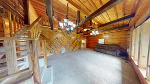 Unfurnished living room with wooden walls, carpet floors, a chandelier, a wooden ceiling with exposed beams, and stairs
