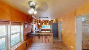 Kitchen with brown cabinets, a peninsula, freestanding refrigerator, light wood-style floors, and ceiling fan