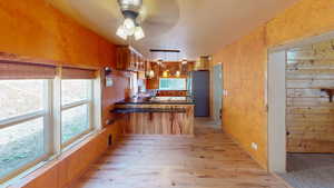 Kitchen featuring a peninsula, dark countertops, brown cabinets, freestanding refrigerator, and light wood-style floors