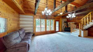 Carpeted living room with a wood stove, wood walls, stairs, a chandelier, and a wooden ceiling with exposed beams