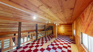 Hallway with light floors, rail lighting, wood walls, wood ceiling, and an upstairs landing