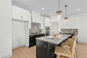 Kitchen featuring two tone cabinets, a center island with sink, decorative light fixtures, light wood-style flooring, and a kitchen breakfast bar