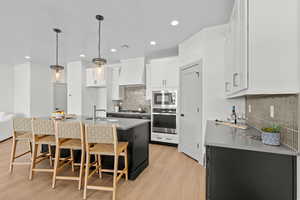 Kitchen with two tone cabinetry, light stone counters, light wood finished floors, stainless steel appliances, and a kitchen bar